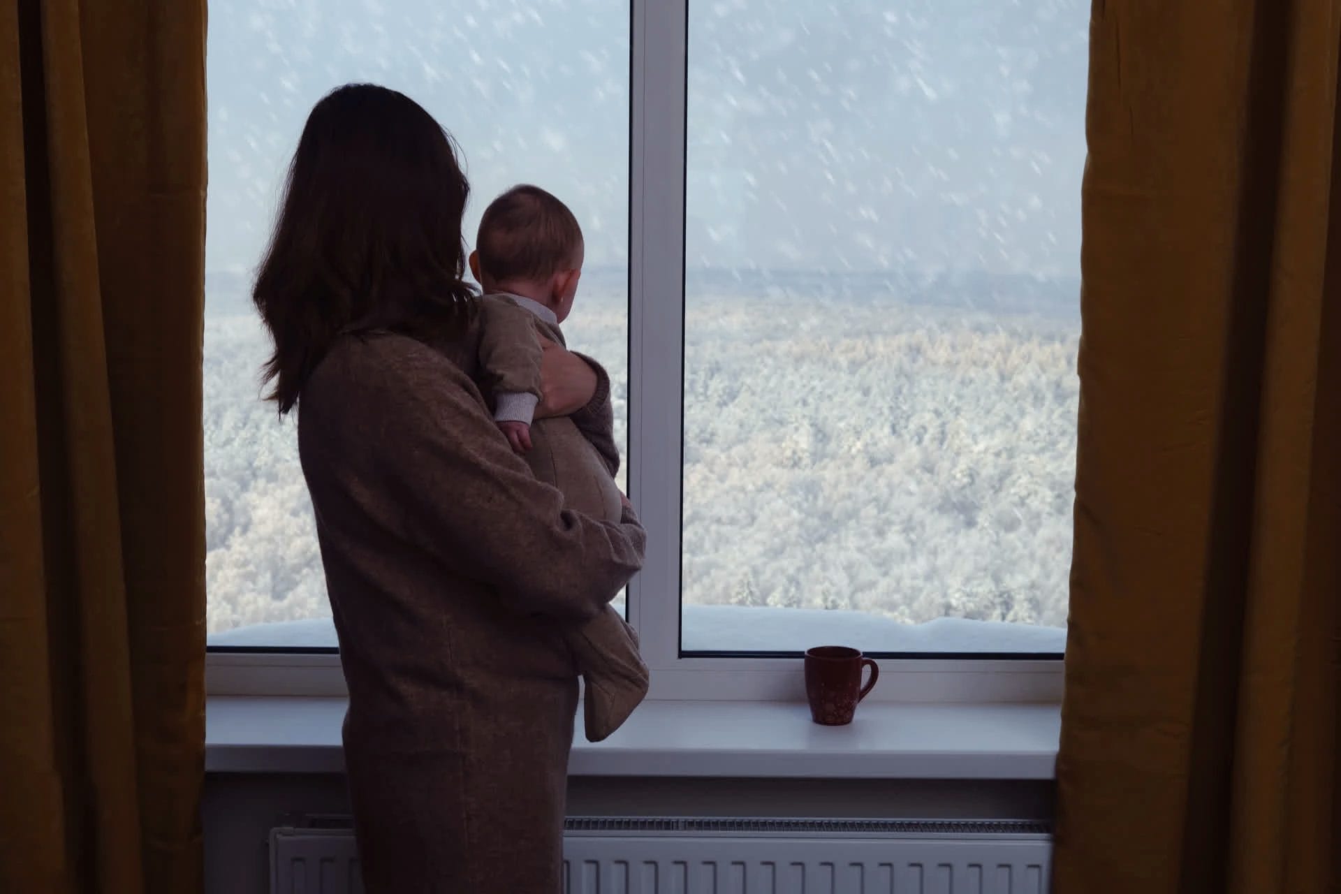 mother and child looking out of made to measure curtains at the snow falling